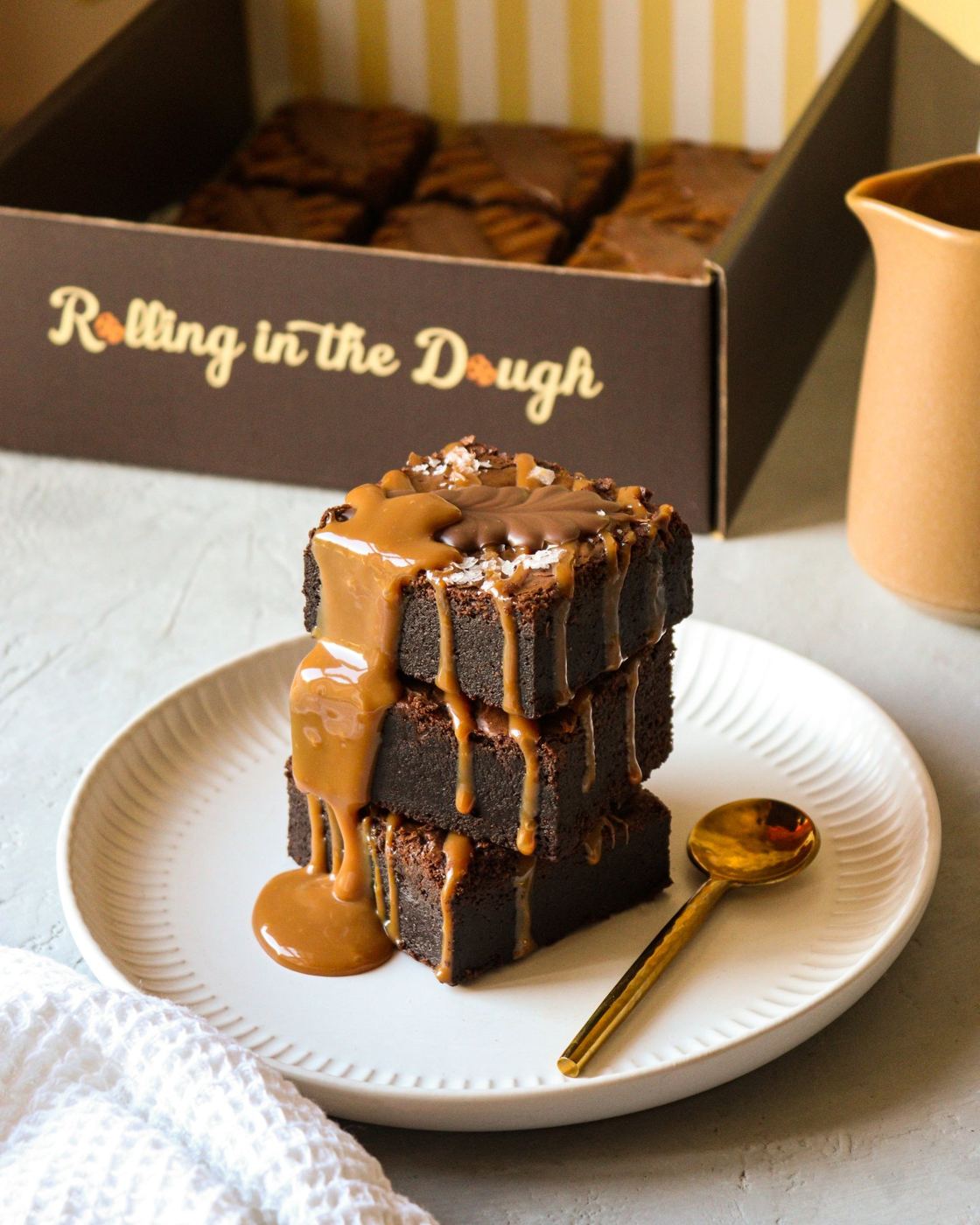 A stack of salted caramel brownies in front of a Rolling in the Dough box