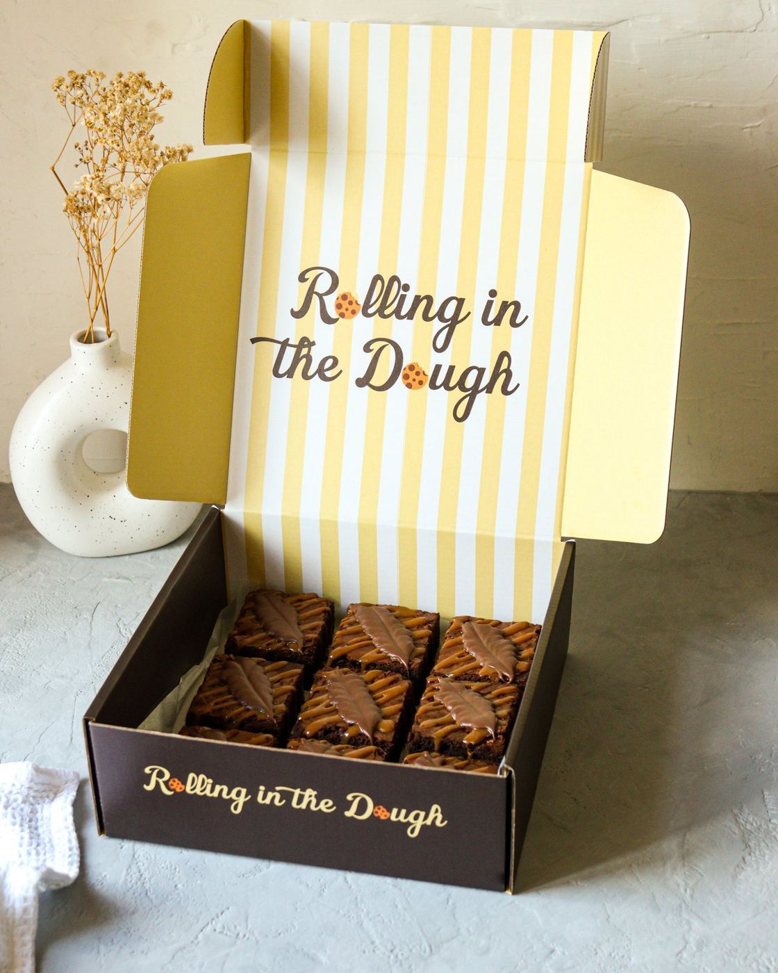An open Rolling in the Dough box of caramel brownies, its lid lined with yellow and white stripes